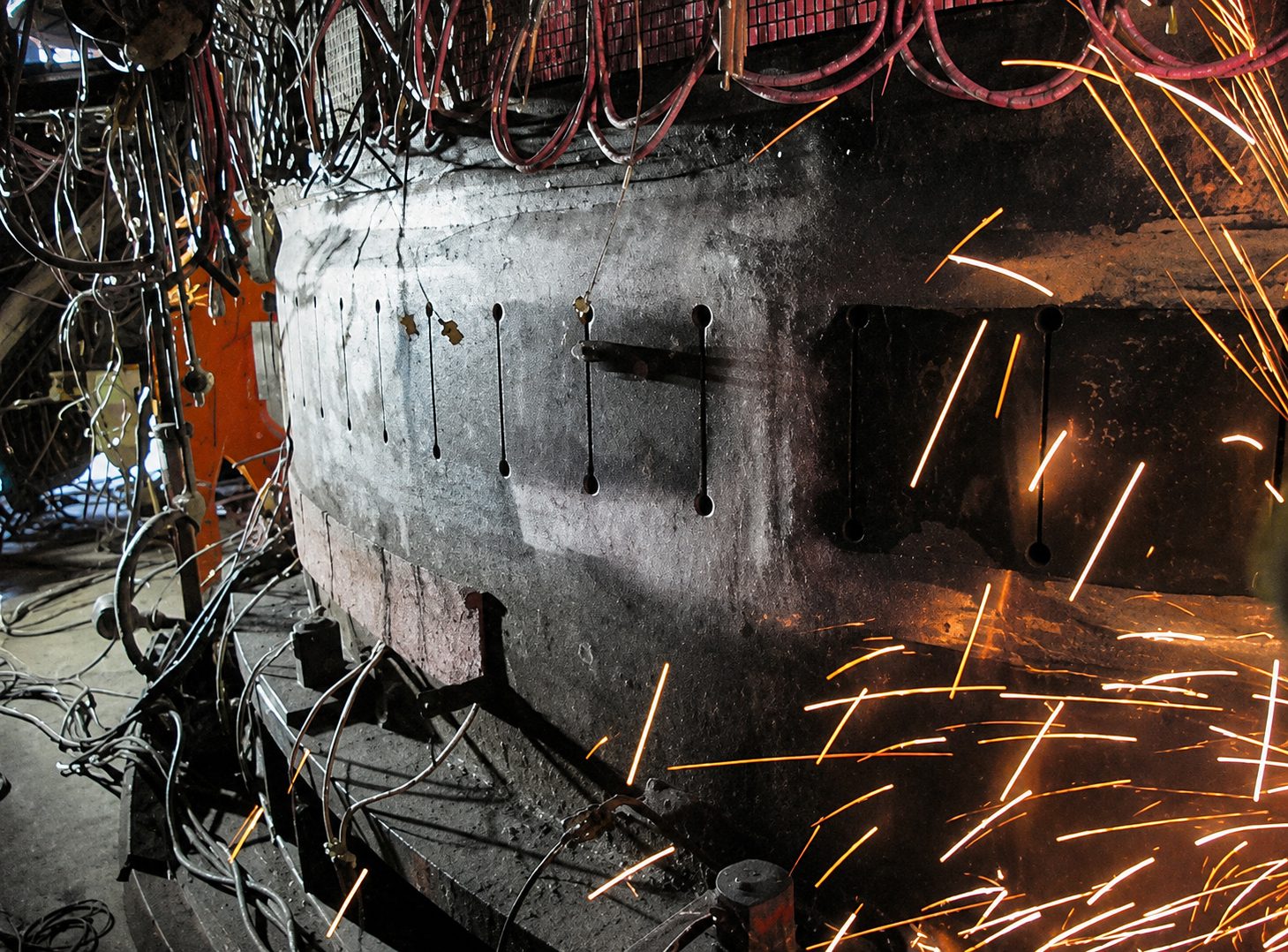 Metal structure with multiple vertical slots being worked on, with sparks flying.