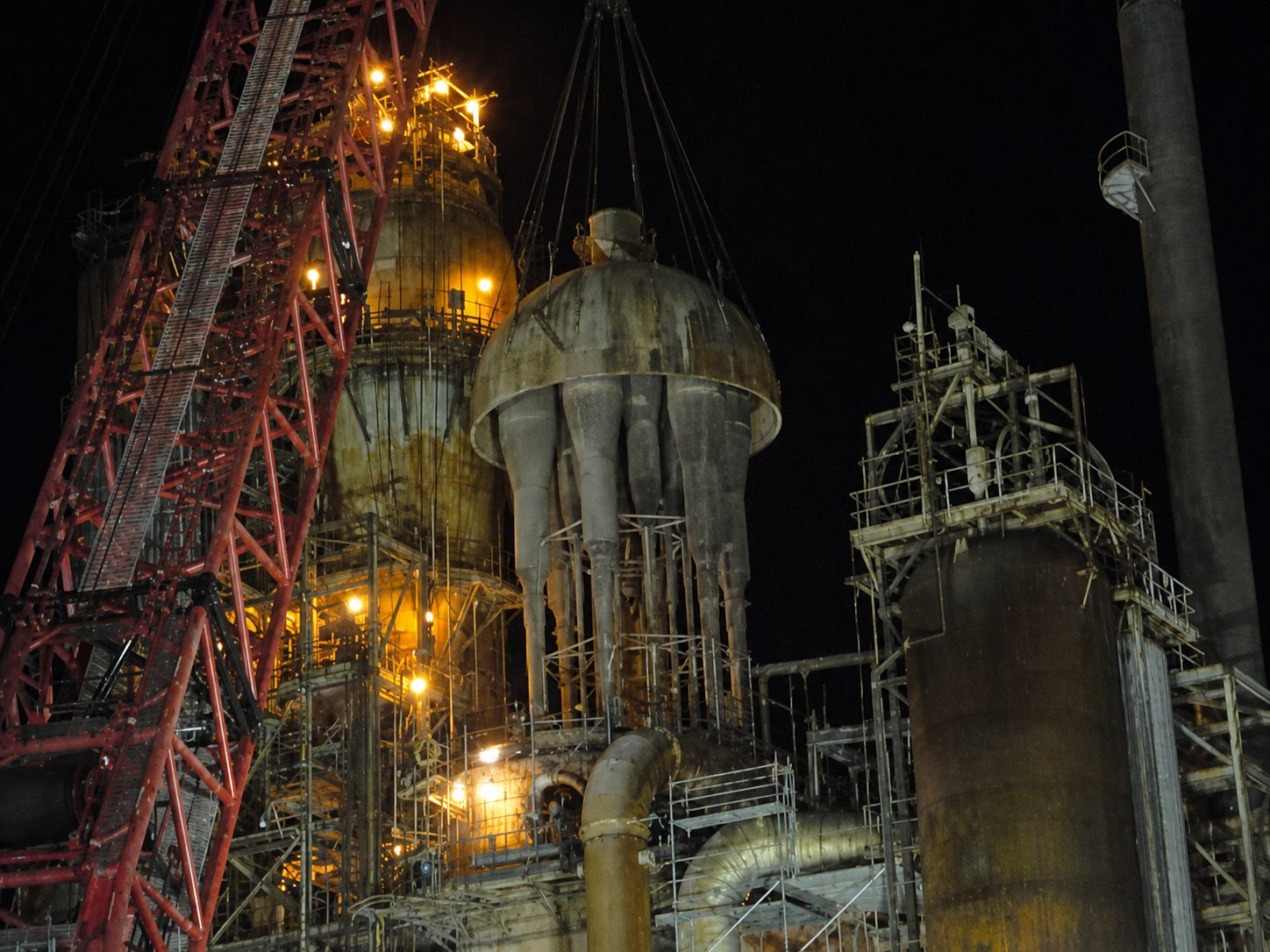 Industrial equipment being lifted by a crane at night.
