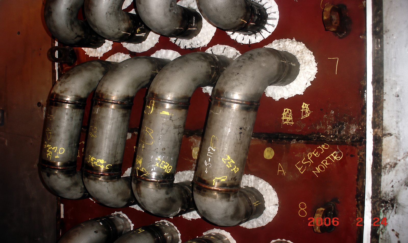 Close-up view of industrial heater piping with welded joints and markings on the metal surface.