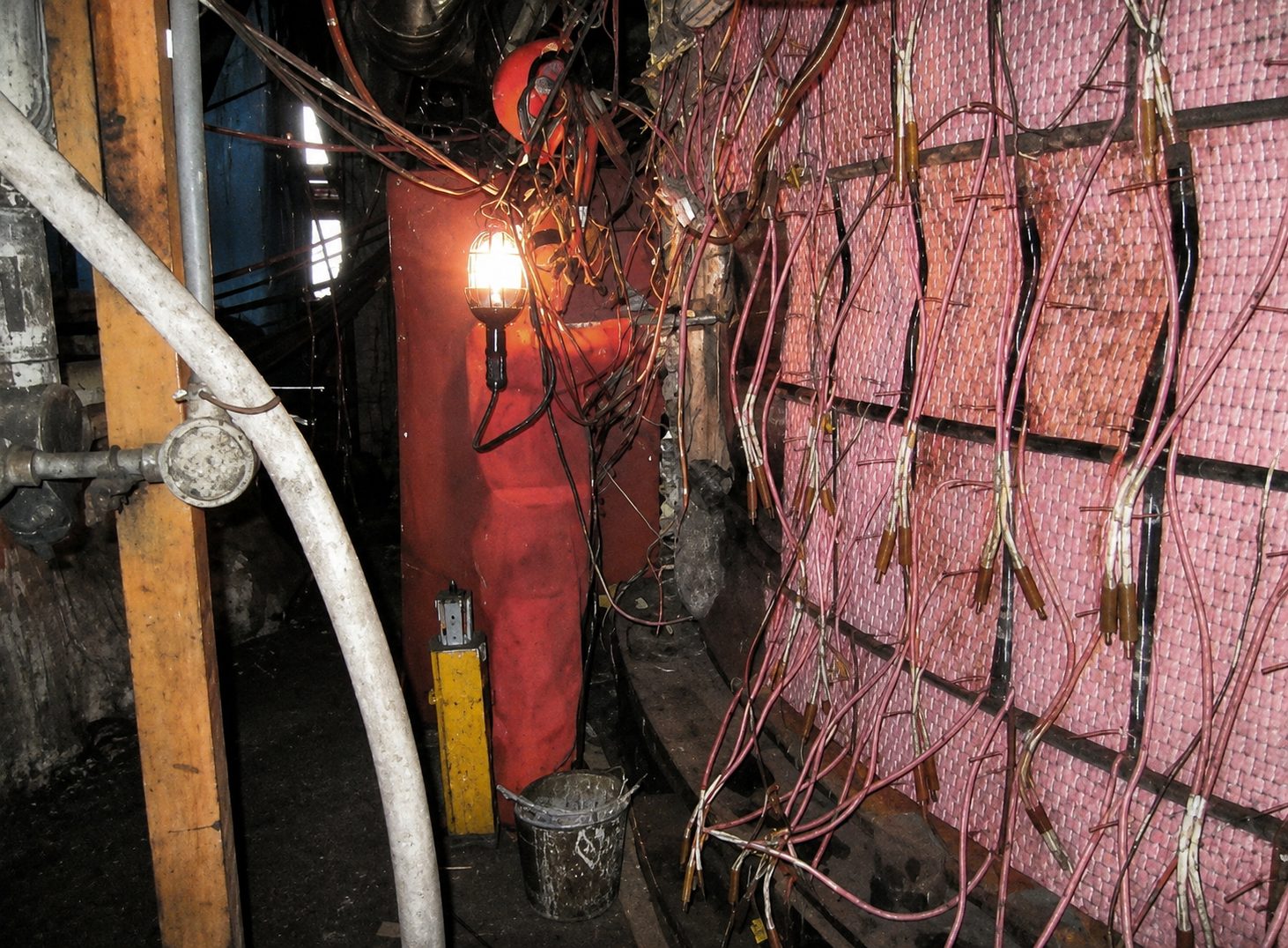 Worker in orange safety gear working on a structure covered in wiring and insulation.