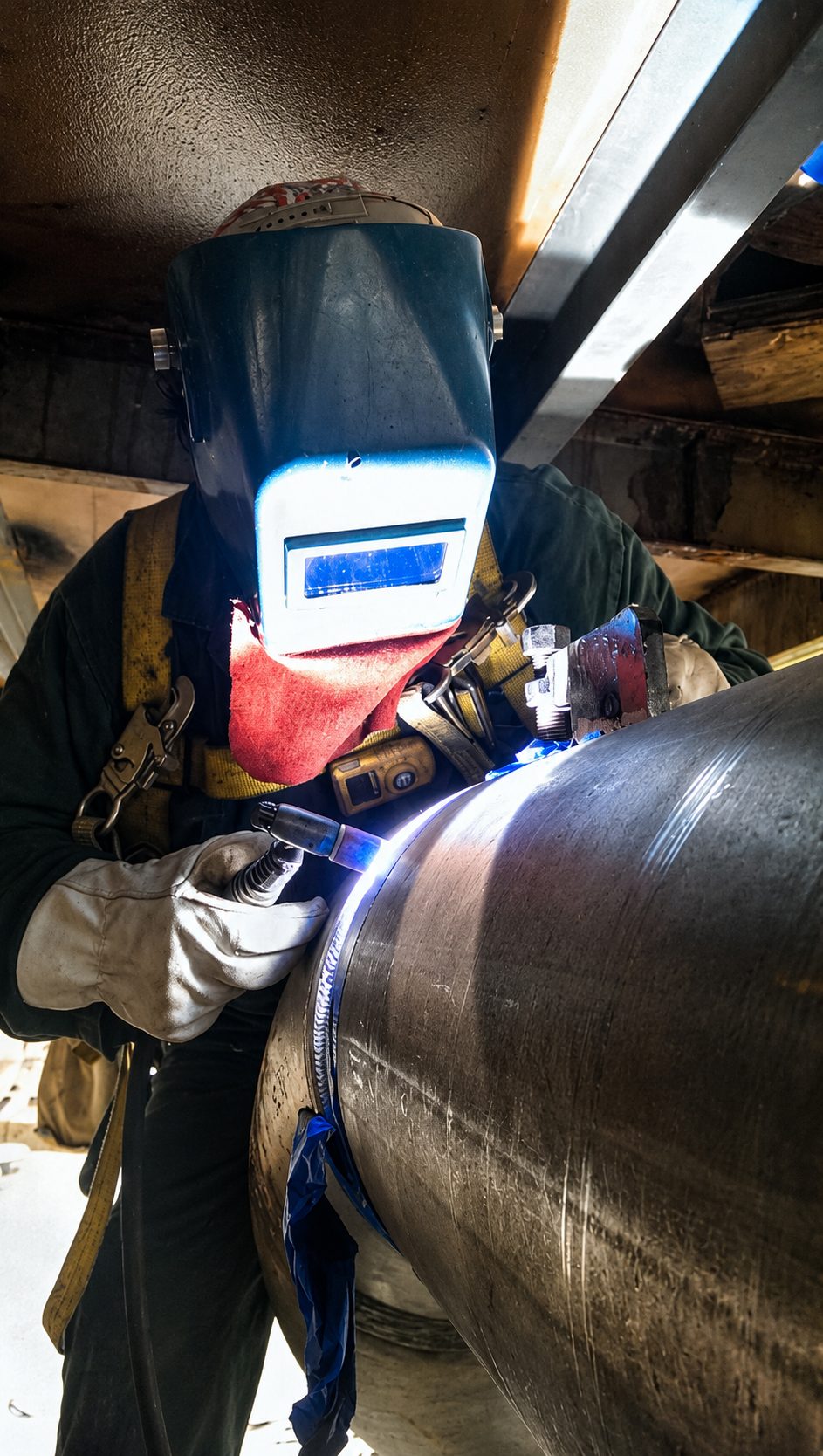 Welder in a protective helmet working on a large metal pipe.