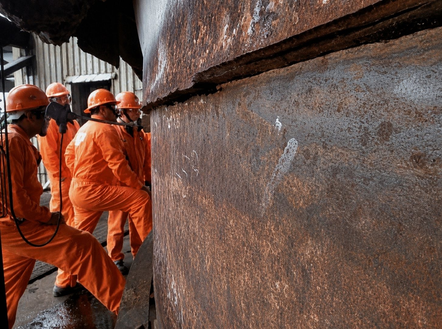 Workers in orange safety gear standing beside a large industrial vessel.