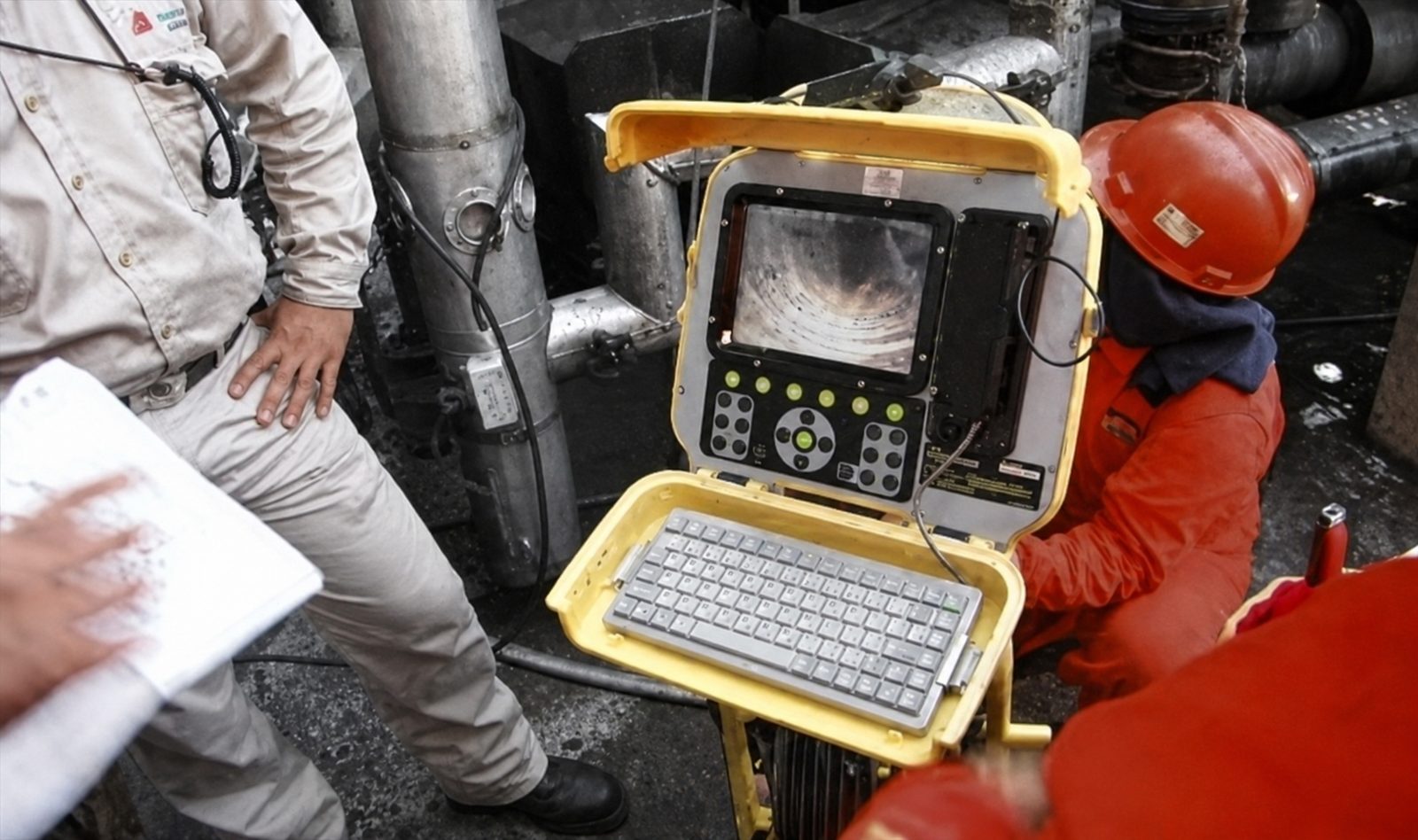 Worker using a portable inspection device with a screen and keyboard in an industrial setting.